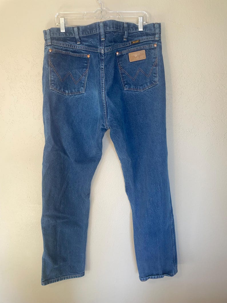 May include: A pair of blue denim jeans with a brown leather patch on the back pocket that says "Wrangler".