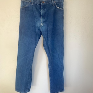 May include: A pair of blue denim jeans hanging on a coat hanger. The jeans have a classic straight leg style and a button fly.