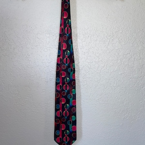 May include: A black silk tie with a geometric pattern of red, blue, and gold circles. The tie is hanging on a wooden hanger.