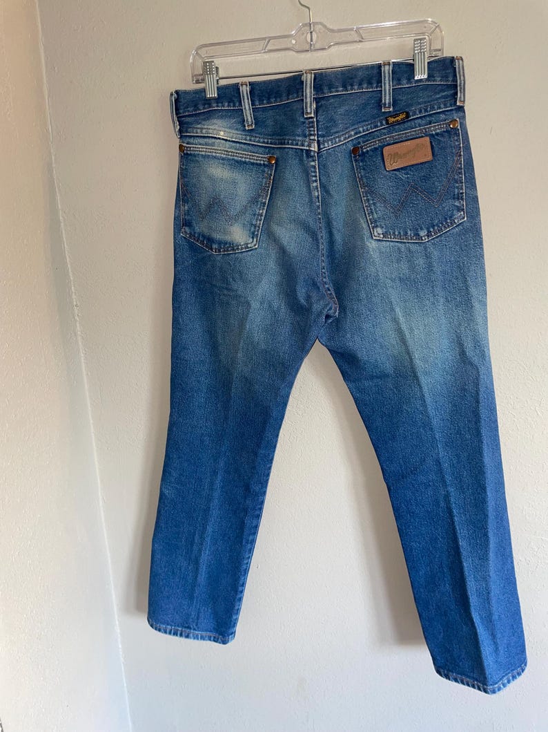 May include: Blue denim jeans with a classic five-pocket design. The jeans have a faded wash and a leather patch with the brand name on the back pocket. The jeans are hanging on a clear plastic hanger.