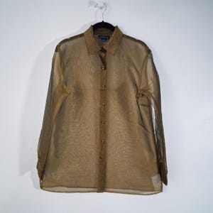 May include: A sheer, long-sleeved button-down shirt in a muted olive green colour. The shirt features a collared neckline and button closures down the front. The fabric appears lightweight and slightly translucent, with a subtle sheen.
