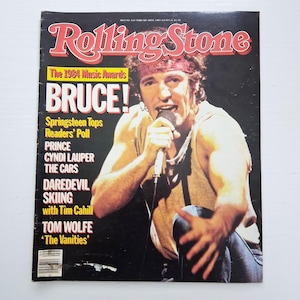 Puede incluir: Una portada de revista Rolling Stone vintage del 28 de febrero de 1985, con Bruce Springsteen usando un pañuelo rojo y una camiseta sin mangas color canela mientras canta en un micrófono. El texto incluye The 1984 Music Awards, Bruce! y otros titulares.