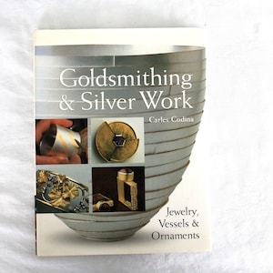 May include: A book titled "Goldsmithing & Silver Work" by Carles Codina. The cover features a silver bowl design and images of jewelry, vessels, and ornaments. The book's subtitle is "Jewelry, Vessels & Ornaments".
