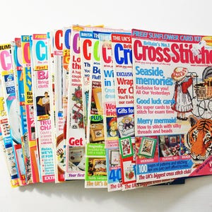Peut inclure: Plusieurs magazines colorés, principalement sur le point de croix. Les couvertures présentent des motifs variés, notamment floraux, animaliers et de fêtes. Les magazines sont empilés sur une surface blanche.