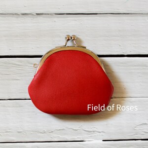 May include: A bright red coin purse with a textured surface and a silver-toned metal kiss-lock clasp closure. The text "Field of Roses" is printed in white in the bottom right corner of the frame, positioned near the base of the red pouch.