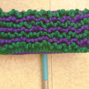 Puede incluir: Una cabeza de fregona de crochet verde y morado unida a un mango de fregona azul.