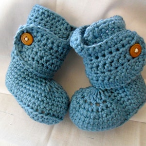 May include: A pair of blue crocheted baby booties with brown buttons. The booties have a fold-over cuff and a textured stitch pattern.