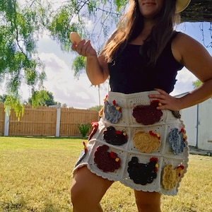 May include: A cream-coloured crochet skirt featuring a grid pattern of individual appliqu&eacute;s shaped like chickens in various colours including black, brown, tan, and blue, each with a small red comb detail, worn with a plain black tank top.