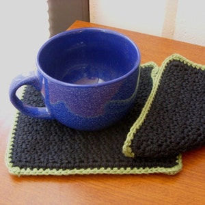 May include: A blue ceramic mug with a speckled finish sits on a black and green crocheted coaster.