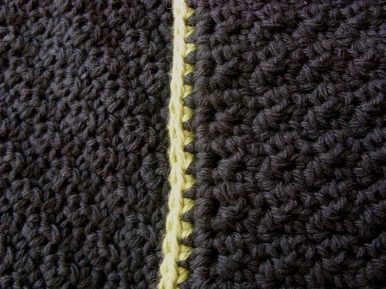 May include: Close-up of black and yellow crocheted fabric. The fabric is made with a single crochet stitch and has a textured look.