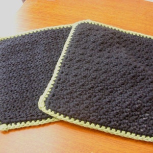 May include: Two black crocheted pot holders with a green crocheted border.