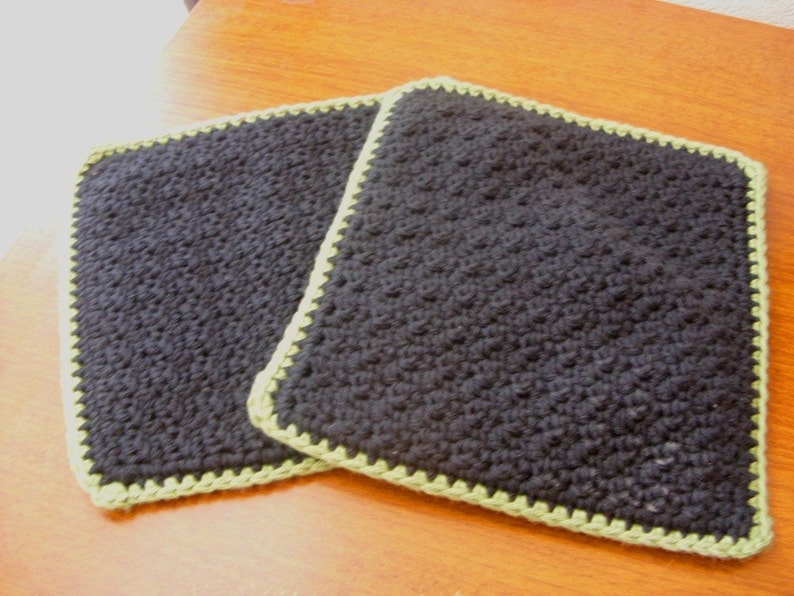 May include: Two black crocheted pot holders with a green crocheted border.