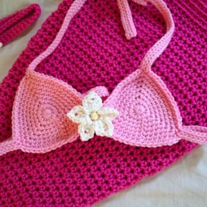 May include: A pink crocheted mermaid tail with a matching pink and white crocheted top and a white flower accent.