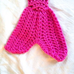 May include: A pink crocheted mermaid tail with a pointed end. The tail is made with a single crochet stitch and has a textured appearance.