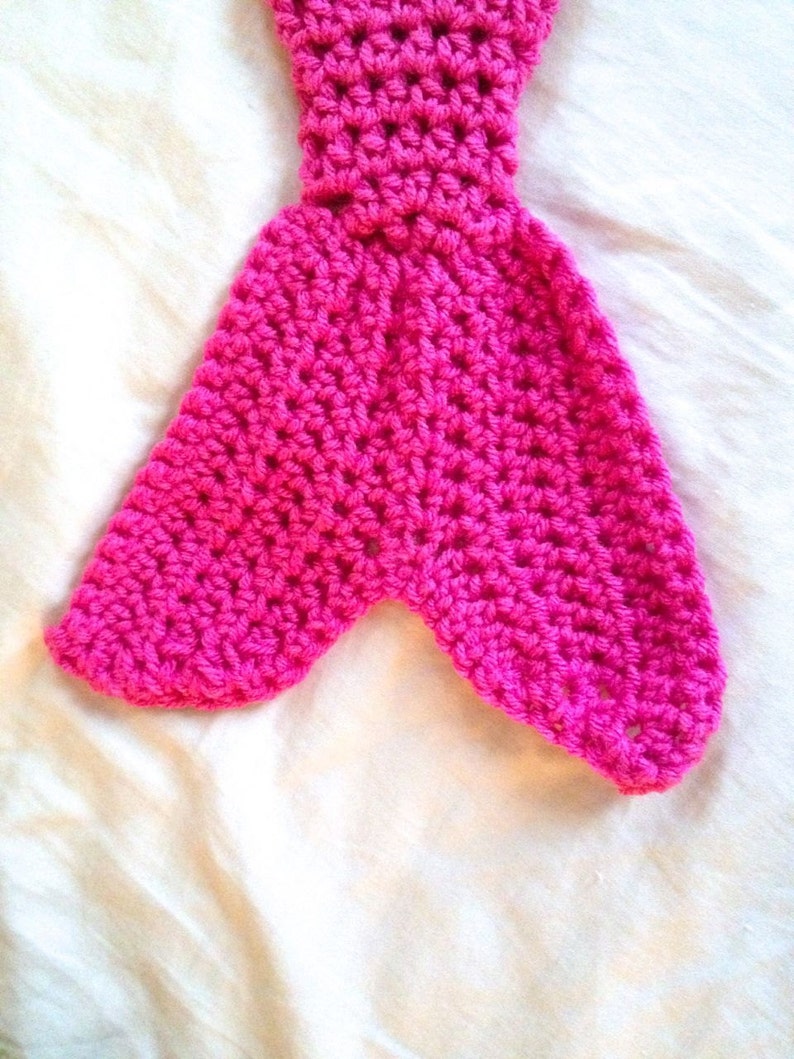 May include: A pink crocheted mermaid tail with a pointed end. The tail is made with a single crochet stitch and has a textured appearance.