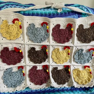 May include: A cream-coloured crocheted wall hanging featuring twelve square panels, each decorated with a textured chicken applique in various colours including yellow, grey, maroon, and brown, each with a small red and yellow comb detail.