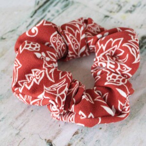 May include: A red and white patterned scrunchie. The scrunchie is made of a soft, stretchy fabric and has a white floral design.