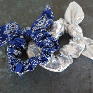 May include: Three hair scrunchies, one silver with glitter and two blue with a white pattern.