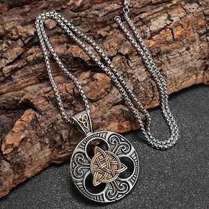 May include: A silver chain necklace with a round pendant featuring a Celtic knot design in gold. The pendant has a detailed, intricate pattern.