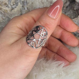 Könnte beinhalten: Ein silberner Ring mit einem Pentagramm-Design. Der Ring ist aus Metall gefertigt und hat ein detailliertes Design. Der Ring wird am Daumen getragen.