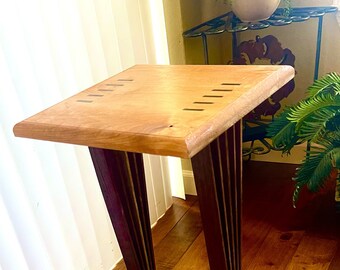 May include: A wooden side table with a light wood top and dark wood legs. The legs are made of multiple pieces of wood that are joined together to create a unique design.