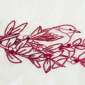 Pode incluir: Desenho bordado de um pássaro empoleirado em um galho com bagas vermelhas. O desenho é feito em fio vermelho escuro sobre um fundo branco.