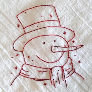 May include: Red embroidered snowman with a top hat and scarf on a white background. The snowman has a carrot nose and a smiling face.
