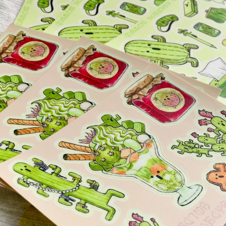 Pode incluir: Um conjunto de adesivos com ilustra&ccedil;&otilde;es de cactos, potes de geleia e uma sobremesa verde em um copo. Os adesivos s&atilde;o impressos em um fundo bege claro.