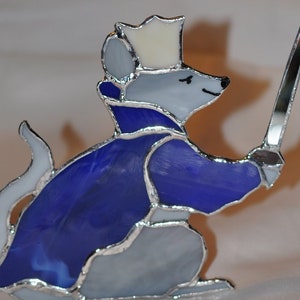 May include: A stained glass mouse wearing a blue cape and a crown, holding a sword. The mouse is made of clear and opaque glass, with silver foil accents.