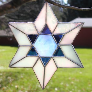May include: A white and blue stained glass star of David ornament with a silver frame.