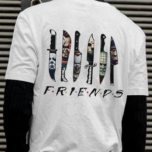 May include: White t-shirt with a graphic of seven knives, each with a different horror movie character's face on the blade. The text "FRIENDS" is printed below the knives.