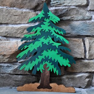 Könnte beinhalten: Ein Holzpuzzle eines grünen Kiefernbaums mit braunem Stamm und Sockel. Der Baum besteht aus vielen ineinandergreifenden Teilen.