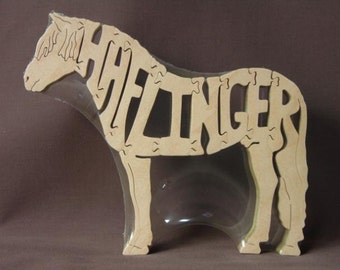 May include: A wooden horse puzzle with the word "HAFLINGER" spelled out on its body. The puzzle is made of light brown wood and is in a clear plastic bag.