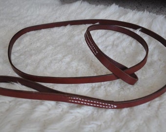 May include: A brown leather leash with white stitching. The leash is folded in half and has a loop at one end.