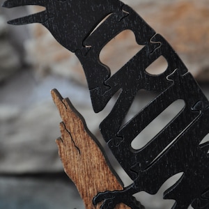 May include: A black wooden crow perched on a branch, the crow is made of interlocking puzzle pieces.