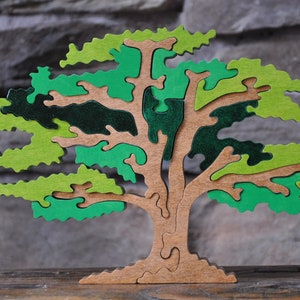 May include: A wooden tree puzzle with green and brown painted leaves. The puzzle is made of multiple pieces that fit together to form the shape of a tree.