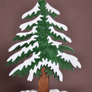May include: A wooden Christmas tree puzzle with green branches and white snow accents. The tree is standing on a white base.
