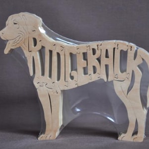May include: A wooden puzzle of a dog, with the word "Ridgeback" spelled out in the dog's body. The puzzle is made of natural wood and is packaged in clear plastic.