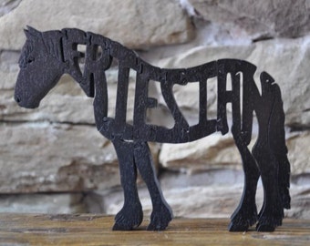 May include: Black wooden horse silhouette with the name "FRIESIAN" cut out of the body. The horse is standing on a wooden surface.