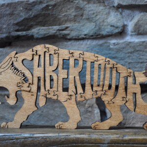 以下が含まれることがあります： サーベルタイガーの形をした木製ジグソーパズル。動物の体に「SABERTOOTH」という単語が書かれています。