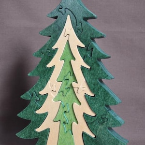 May include: A wooden puzzle in the shape of a green Christmas tree. The tree is made up of multiple pieces that fit together to create a larger tree.