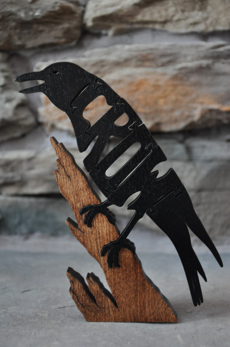 May include: A black wooden crow sculpture with the word "CROW" carved into its body. The crow is perched on a brown wooden branch.
