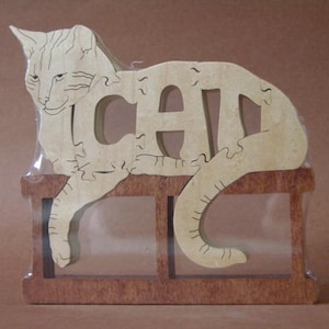 May include: A wooden cat puzzle with the word "CAT" spelled out in the cat's body. The cat is sitting on a wooden platform.