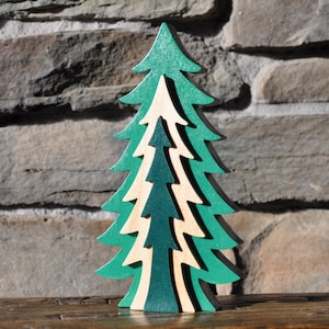 Könnte beinhalten: Ein hölzerner Weihnachtsbaumschmuck mit einem geschichteten Design. Der Baum ist in Grüntönen und Naturholz lackiert.