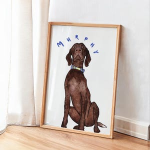 May include: A framed print featuring a brown dog sitting and wearing a light blue collar. The name MURPHY is written in blue capital letters in an arc above the dog's head. The illustration is set against a plain white background.