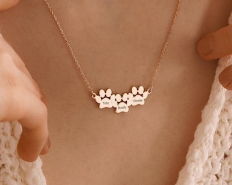 May include: A gold necklace with a paw print charm featuring the names "Max", "Buddy", and "Charlie".