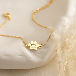 Pode incluir: Uma pulseira de corrente em tom dourado com um pingente central em forma de pata gravado com o nome Molly. A delicada corrente de metal inclui um fecho de mola circular e uma sec&ccedil;&atilde;o de elos de extens&atilde;o ajust&aacute;vel para o pulso.