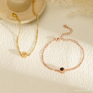 May include: Two gold bracelets with a small round charm. One bracelet is gold and the other is rose gold. The charms have a small black stone in the center.