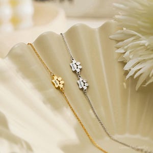 Pode incluir: Duas pulseiras delicadas, uma dourada e outra prateada, cada uma com um pequeno pingente de pata. A pulseira dourada est&aacute; gravada com o nome Molly, enquanto a pulseira prateada apresenta dois pingentes de pata gravados com Buddy e Poppy.