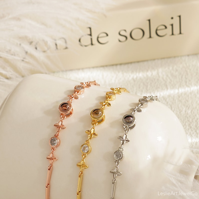 May include: Three delicate bracelets with a floral design and small round stones. The bracelets are in rose gold, gold, and silver.